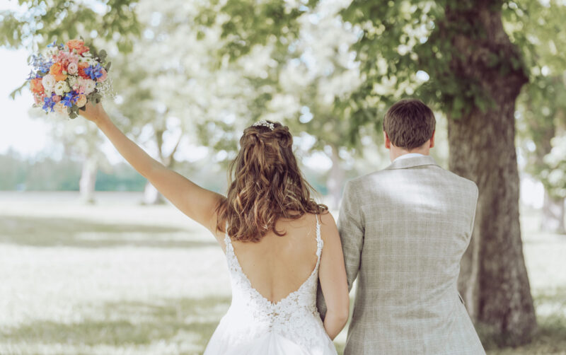 Brautpaar mit Rücken zur Kamera, die Braut hält den Brautstrauß in der linken Hand