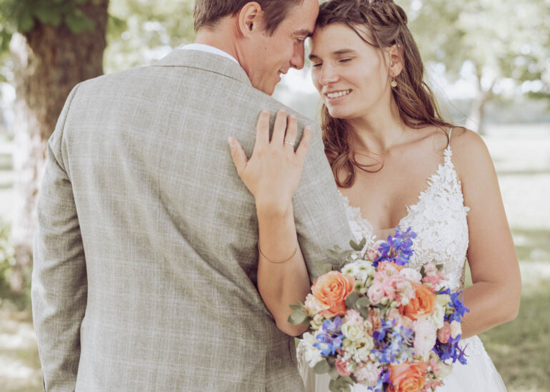 Braut hält sich an Bräutigam fest und hat den Brautstrauß in der anderen Hand