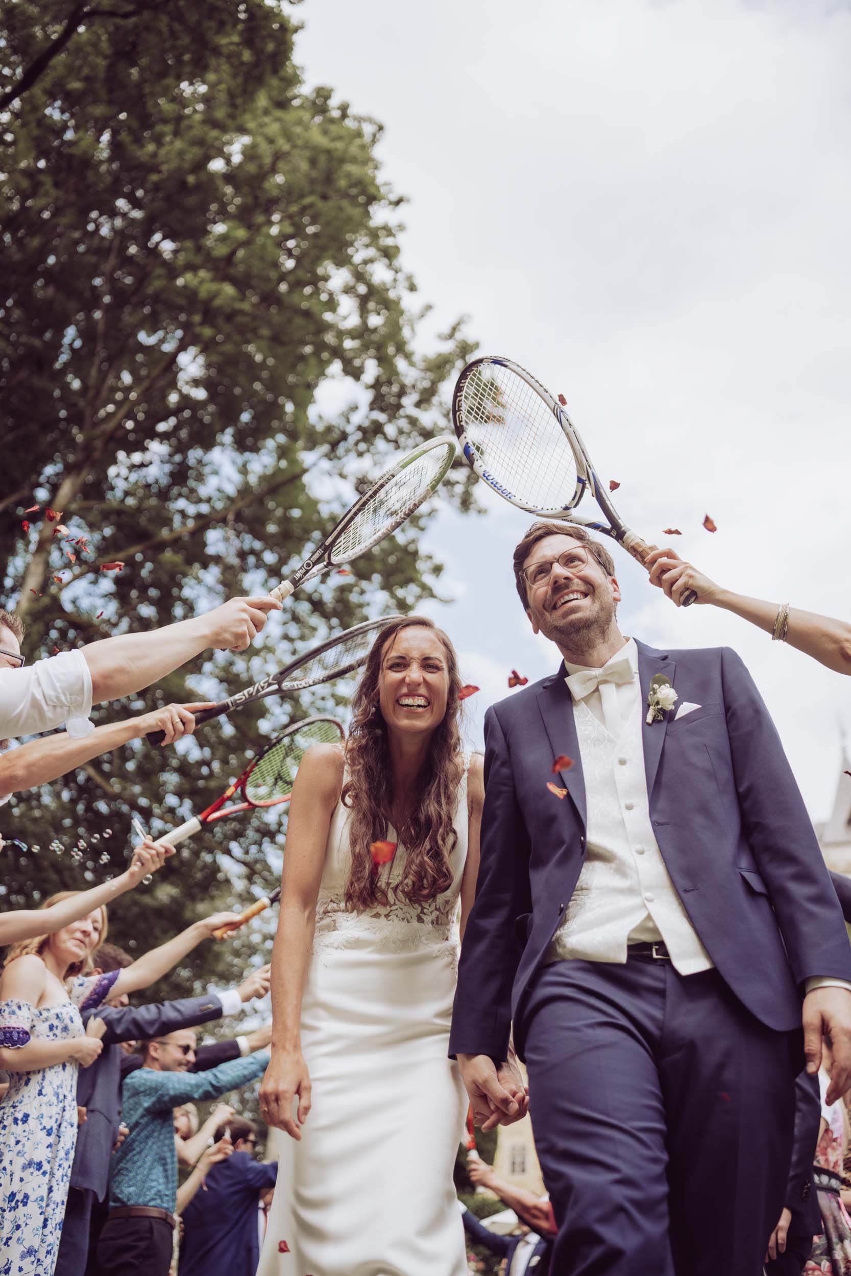 Hochzeitspaar läuft lachend unter Tennisschlägern hindruch