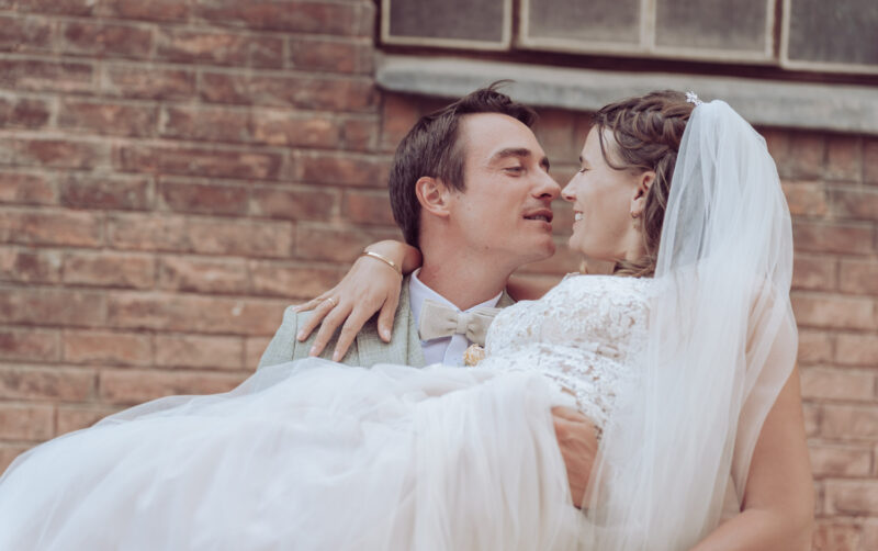 Bräutigam hat die Braut auf dem Armt. Die zwei schauen sich in die Augen