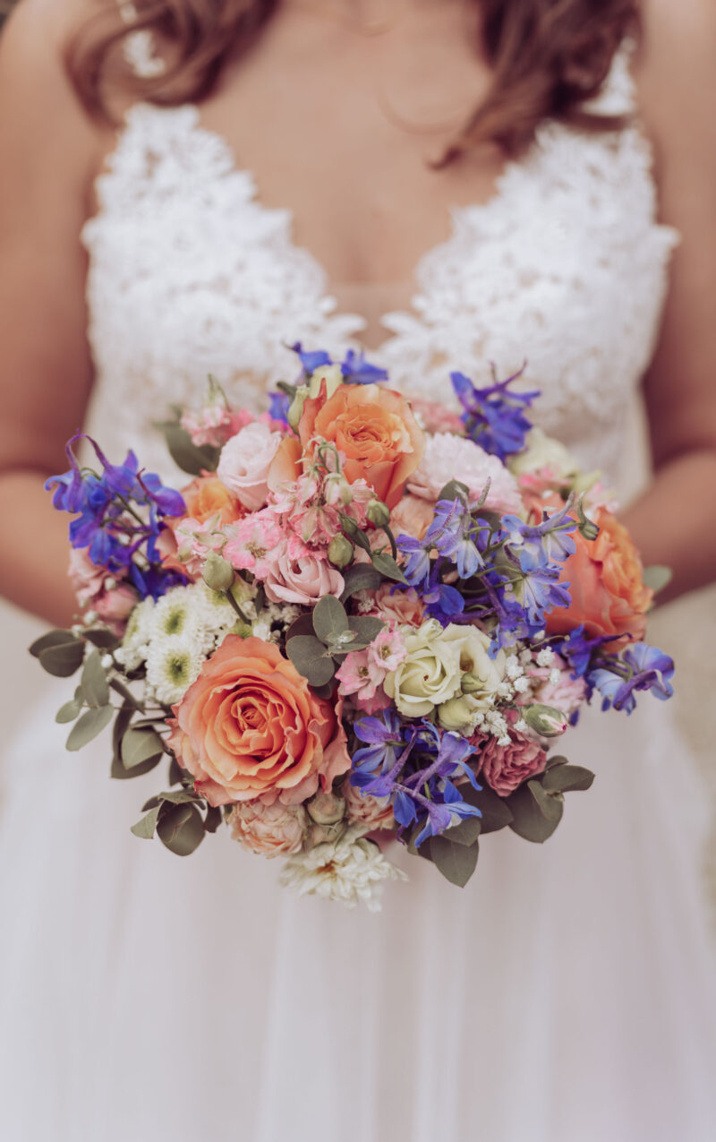 Braut im weißen Kleid hält den bunten Brautstrauß vor sich