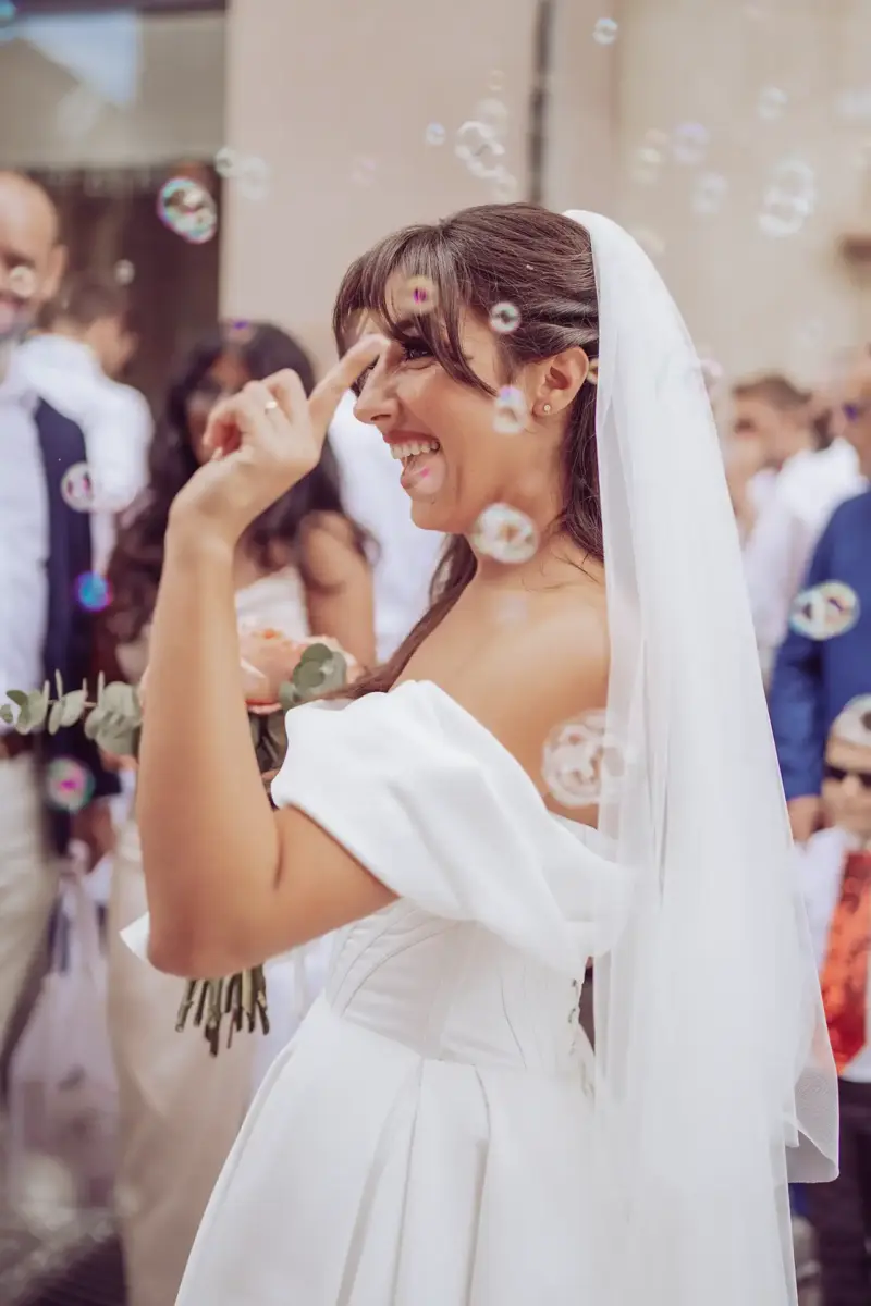 Braut hebt lachend die Hand und ist von Seifenblasen umgeben