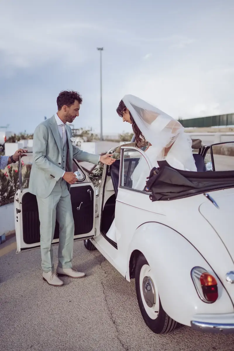 Braut steigt aus weißem Oldtimer Cabrio und nimmt die Hand des Bräutigams