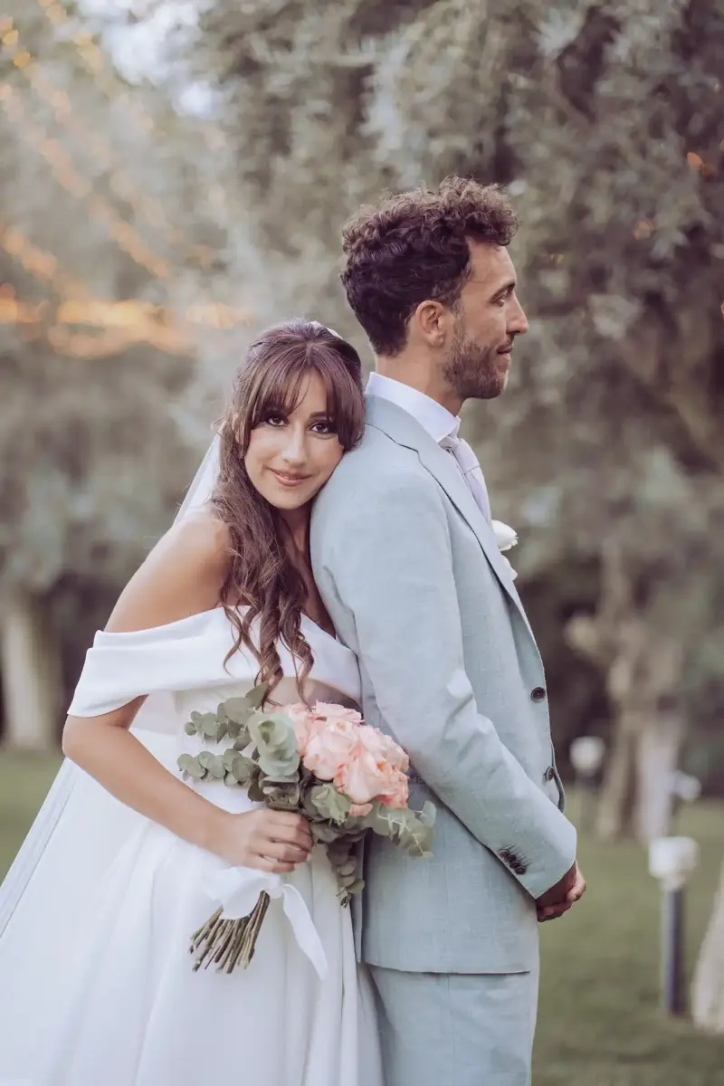 Braut lehnt ihren Kopf an Schulter des Bräutigams und schaut in die Kamera