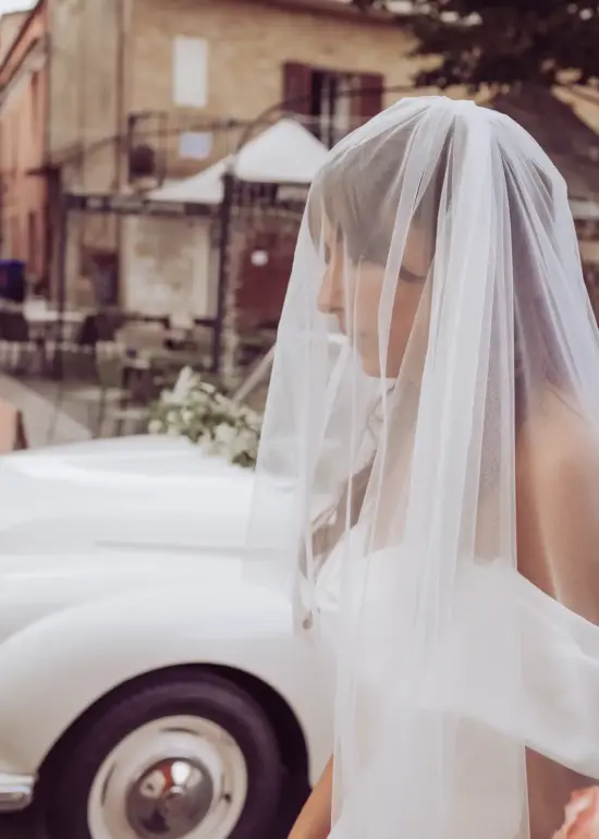 Braut mit Schleier steht vor Cabrio