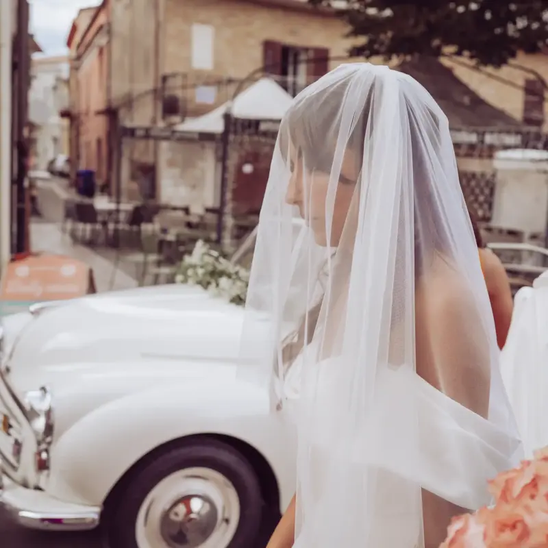 Braut mit Schleier steht vor Cabrio