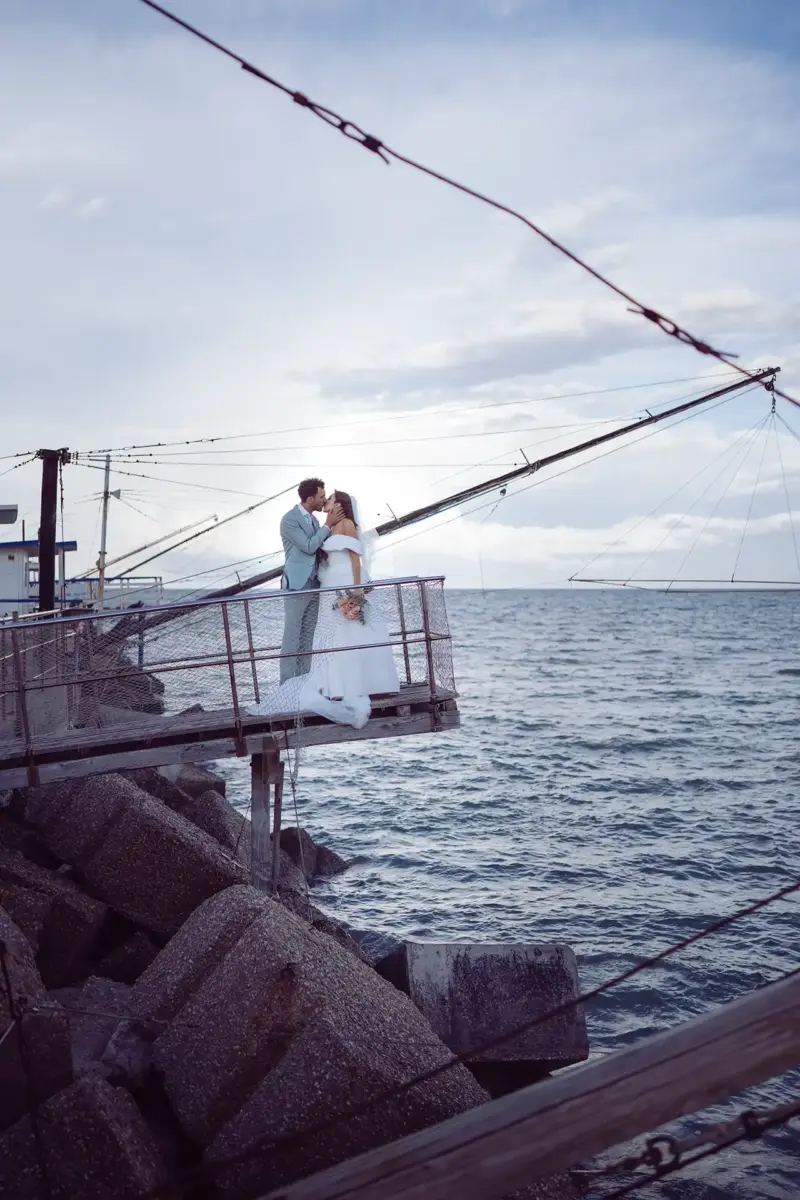 Brautpaar steht auf Steg am Hafen und küsst sich