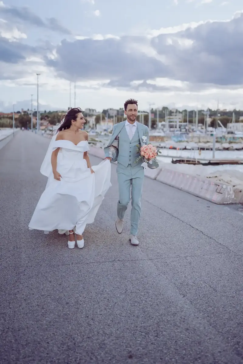 Brautpaar läuft am Hafen, Braut schaut Bräutigam verliebt an, der den Brautstrauß in der Hand hält