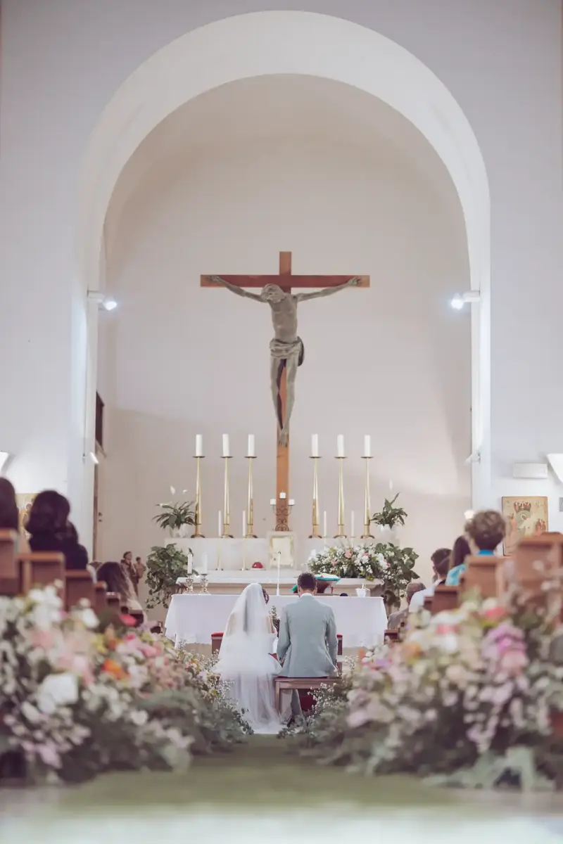 Brautpaar sitzt in der Kirch vor dem Altar mit großem Kreuz Jesu im Hintergrund