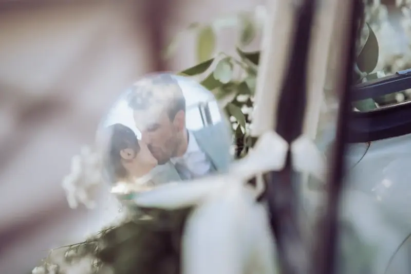Brautpaar küsst sich im Auto und man sieht es im Außenspiegel