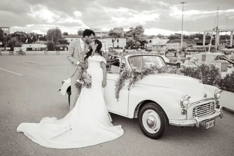 Brautpaar steht vor Oldtimer Cabrio am Hafen und küsst sich, Schwarz-Weiß