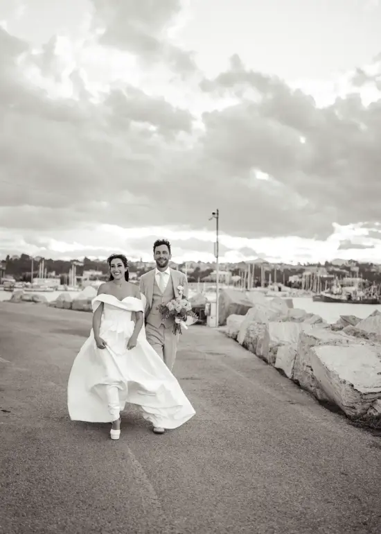 Brautpaar läuft am Hafen lachend auf Kamera zu, Schwarz-Weiß