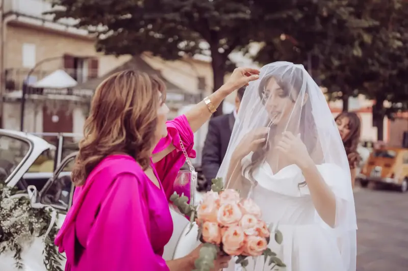 Mutter der Braut mit leuchtendem Kleid richtet den Schleier der Braut