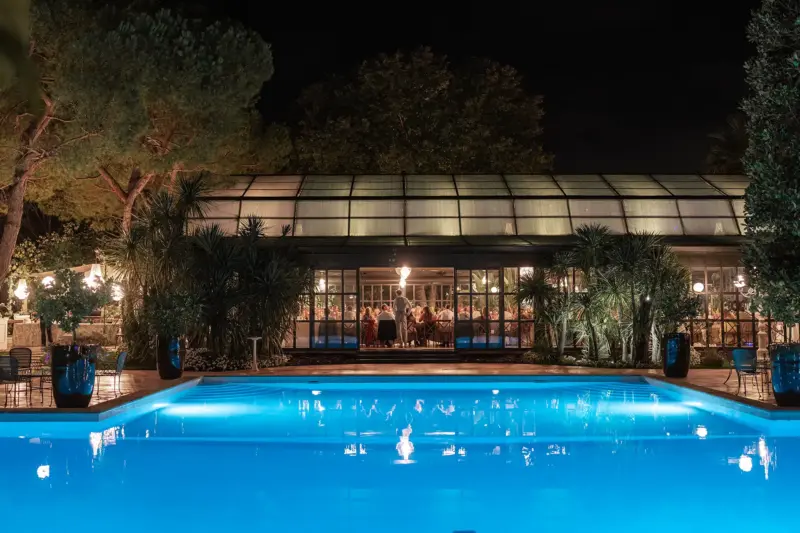 Halle bei Nacht mit Hochzeitsgästen und Pool im Vordergrund