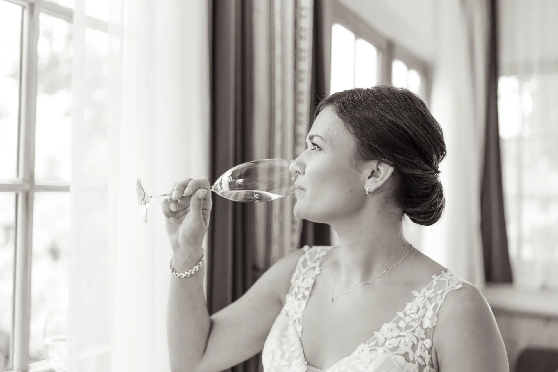 Braut steht am Fenster und trinkt ein Glas Sekt