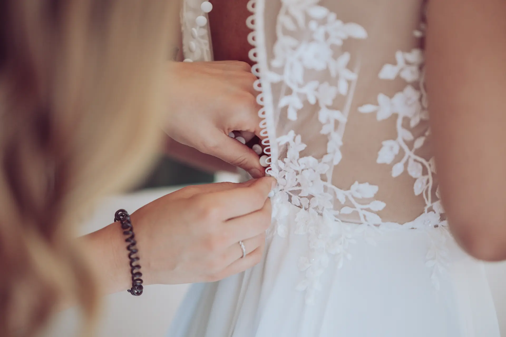 Trauzeugin knöpft das Kleid der Braut am Rücken zu