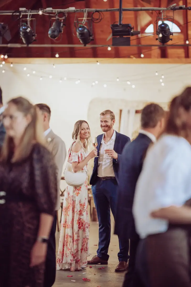 Zwei Hochzeitsgäste lachen aus der Menge in die Kamera