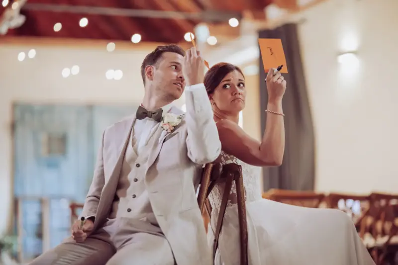 Das Hochzeitspaar sitzt auf Stühlen und hält Schilder hoch