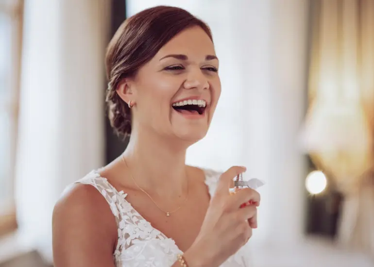 Braut sprüht sich mit Parfüm ein und lacht herzlich