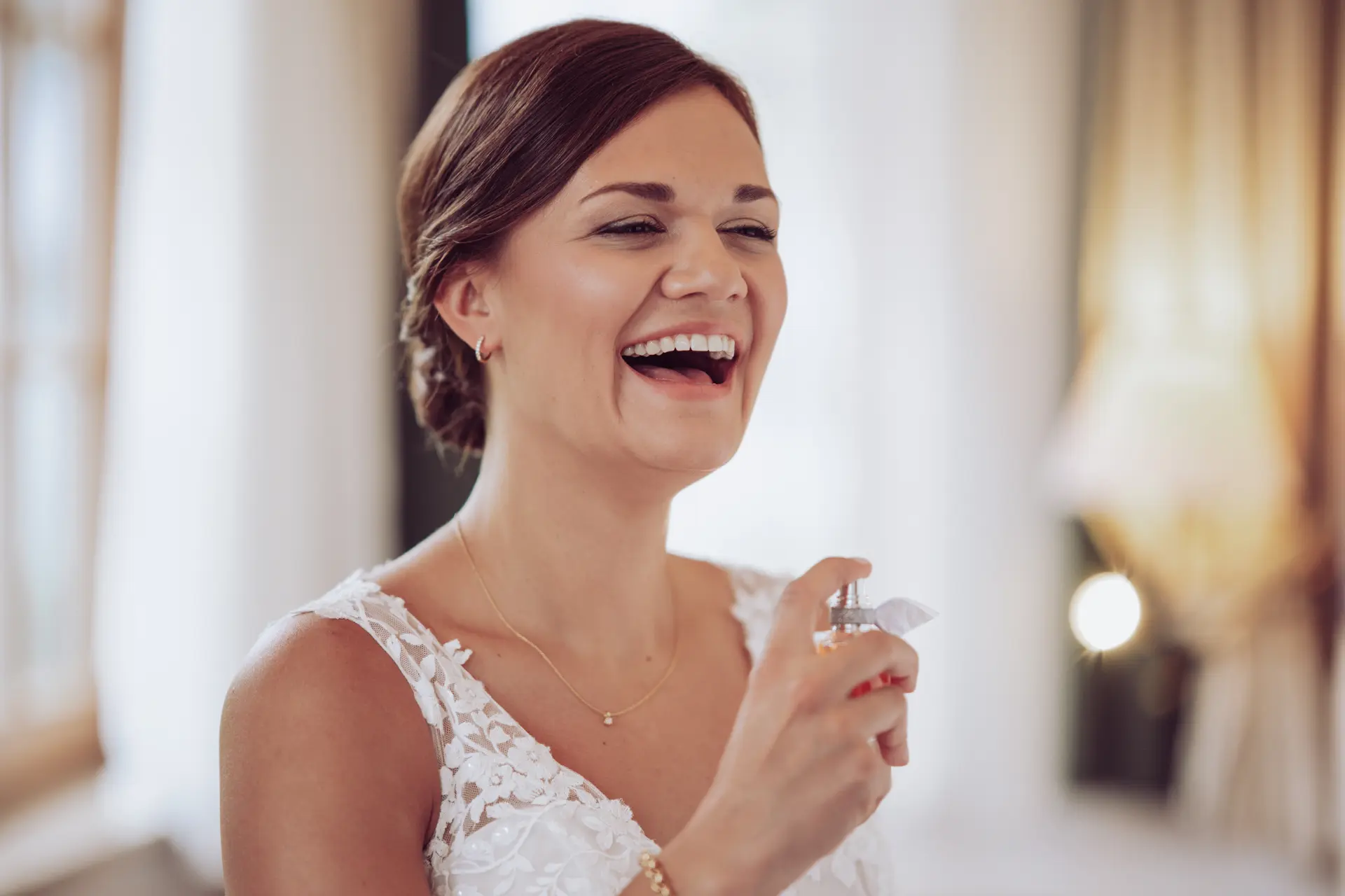 Braut sprüht sich mit Parfüm ein und lacht herzlich