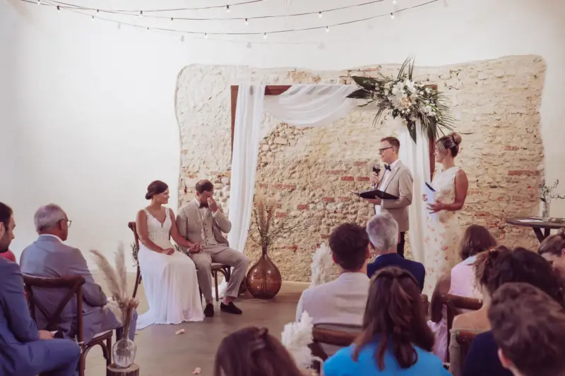 Weinender Bräutigam sitzt neben der Braut während der Trauung in der Remise Schloß Fußberg